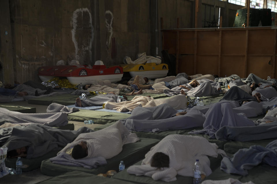Survivors of a shipwreck sleep in a warehouse at the port in Kalamata town, about 240 kilometers (150 miles) southwest of Athens, Wednesday, June 14, 2023. A fishing boat carrying migrants trying to reach Europe capsized and sank off Greece on Wednesday, authorities said, leaving at least 79 dead and many more missing in one of the worst disasters of its kind this year. (AP Photos/Thanassis Stavrakis)