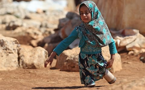 Maya walks on legs made of tin cans in a refugee camp in Idlib - Credit: AAREF WATAD/AFP