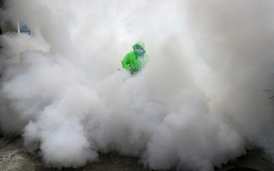 A worker wearing a protective suit disinfects a village as a precaution against the spread of the coronavirus in Manila, Philippines - Aaron Favila/AP