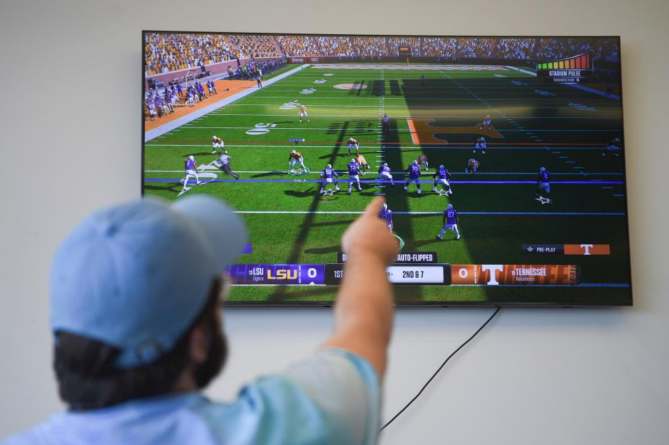 Knox News reporter Keenan Thomas points to the TV in the Knox News office while playing College Football 25.