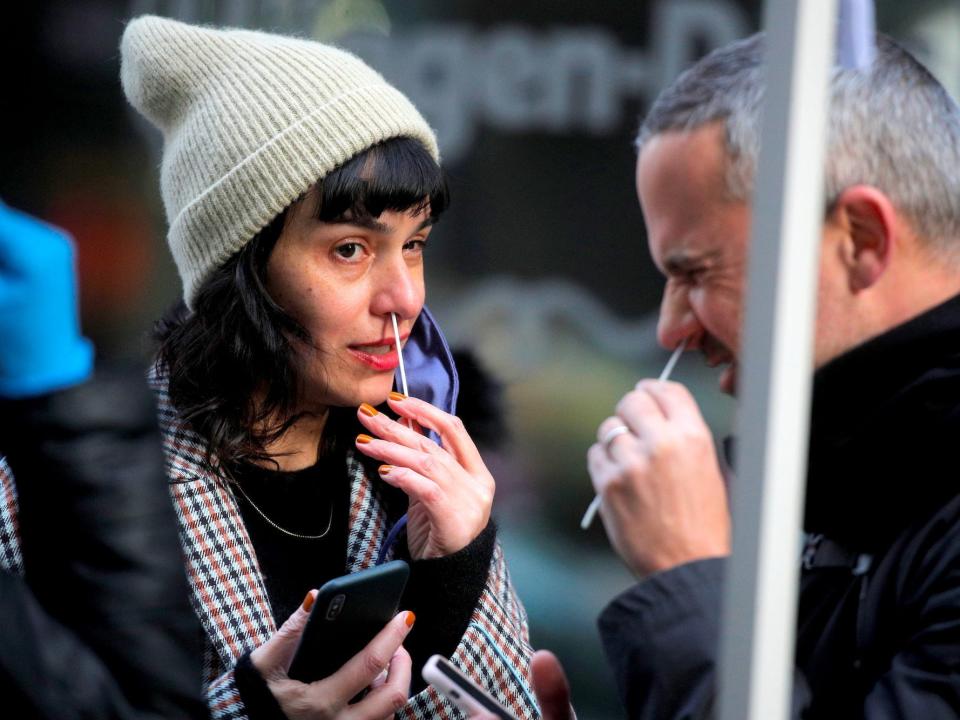 A man whinces while swabbing his nose for a covid test in New York City, USA on December 7, 2021, while a woman also swabbing her nose looks at him,