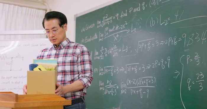 Professor packing up a box with a chalkboard behind him