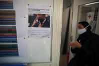 In this Friday, June 12, 2020 photo, an employee cleans her hands as she walks by a poster of director Thomas Delise's message to employees showing a picture of Emmanuel Macron wearing a mask in Chanteclair Hosiery, a French knitwear clothing manufacturer in Saint Pouange, east of Paris. The French praised the altruism of luxury goods companies such as LVMH, Kering and Chanel for diverting their production facilities to make millions of face masks for the public during the peak of their country's coronavirus outbreak. Now, the companies that helped France avoid a dangerous shortage say they need help unloading a surplus of 20 million washable masks. (AP Photo/Francois Mori)