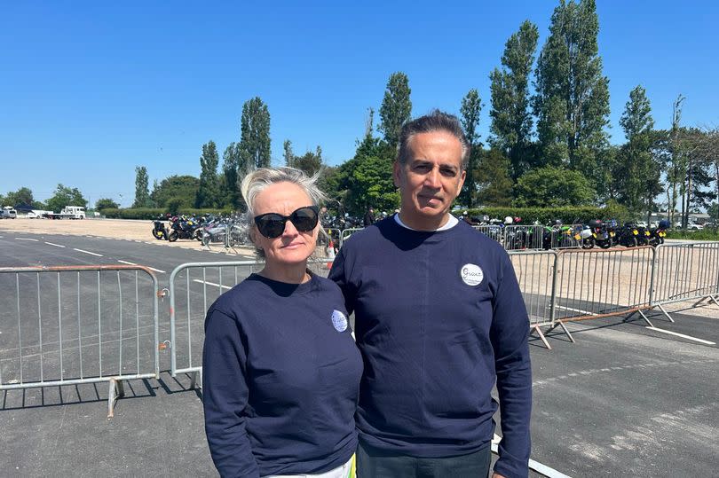 Sanjoy and Sinead O'Malley-Kumar wearing Grace O'Malley-Kumar foundation shirts, with blue sky in front of parked motorbikes and Newark Showground