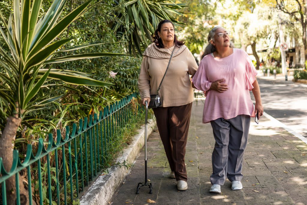 Two women walk along a path. One women is using a cane.