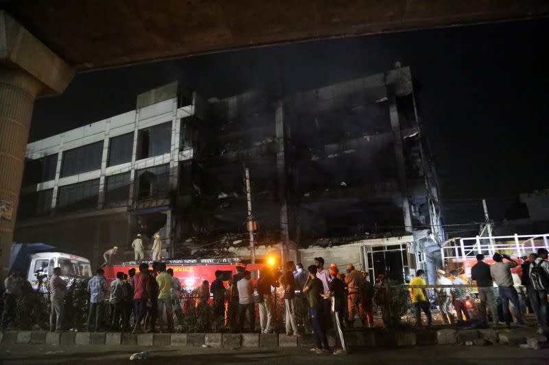 Rescue members and onlookers stand as fire fighters douse a fire that broke out at a commercial building in Delhi's western suburb