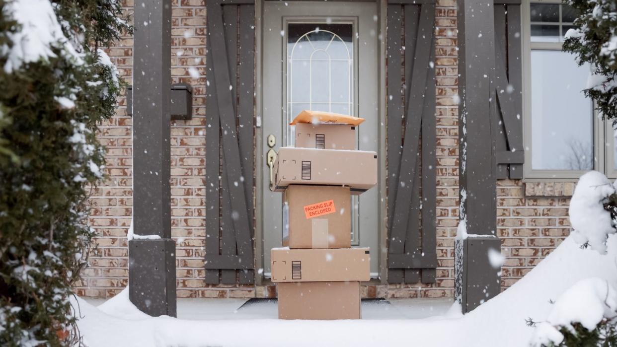 pile of delivered boxes being left outside at front door during snowstorm in winter