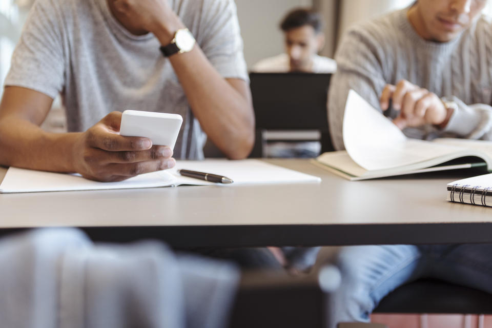 Midsection of male student using smart phone while sitting at desk in classroom