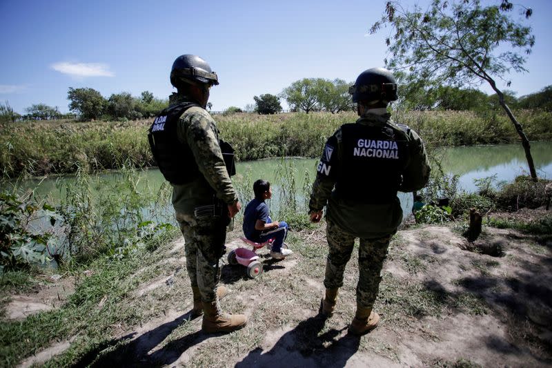 FILE PHOTO: A migrant boy, an asylum seeker sent back to Mexico from the U.S. under the "Remain in Mexico" program officially named Migrant Protection Protocols (MPP), is seen near two members of the Mexican National Guard at a provisional campsite near th