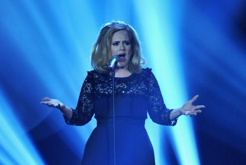 adele holding her arms out and singing into a microphone on a stand