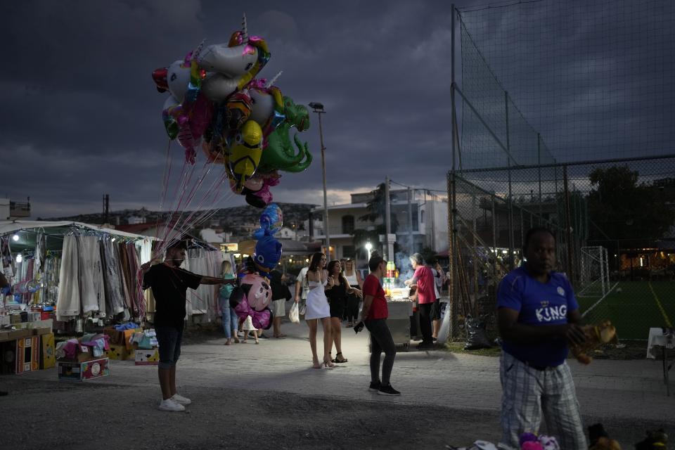 Vendors sell their goods at a flea market as visitors walk during a festivity, known as Panigiri, in Hasia, northwestern Athens, Greece, Sunday, Aug. 14, 2022. The Dormition of the Virgin Mary (or Mother of God as the Greeks usually refer to her) is celebrated on Aug. 15. The religious event is coupled with midsummer festivities, known as Panigiria, that often last more than a day with music, culinary feasts and, in many cases, flea markets. (AP Photo/Thanassis Stavrakis)