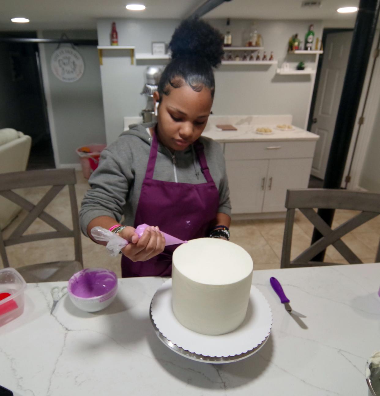 Fourteen-year-old Serina Ribeiro of Brockton begins the process of creating what she calls a "drip cake" by applying icing along the rim of the base cake and letting it drip over the side, on Thursday, March 3, 2022.