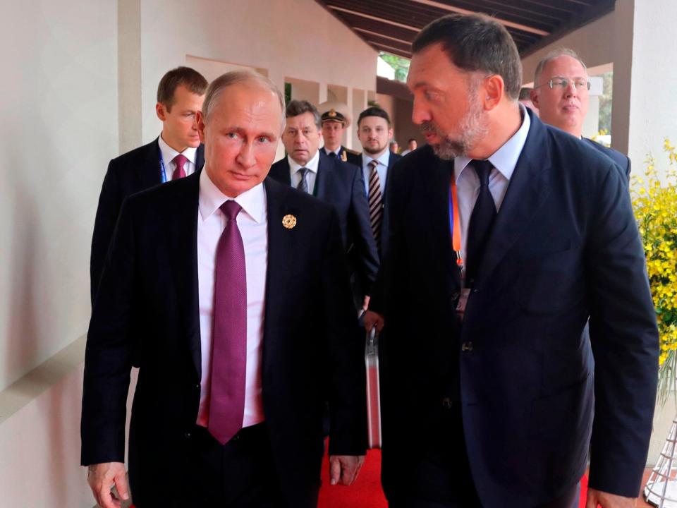 Vladimir Putin walks beside Oleg Deripaska with several men behind them.