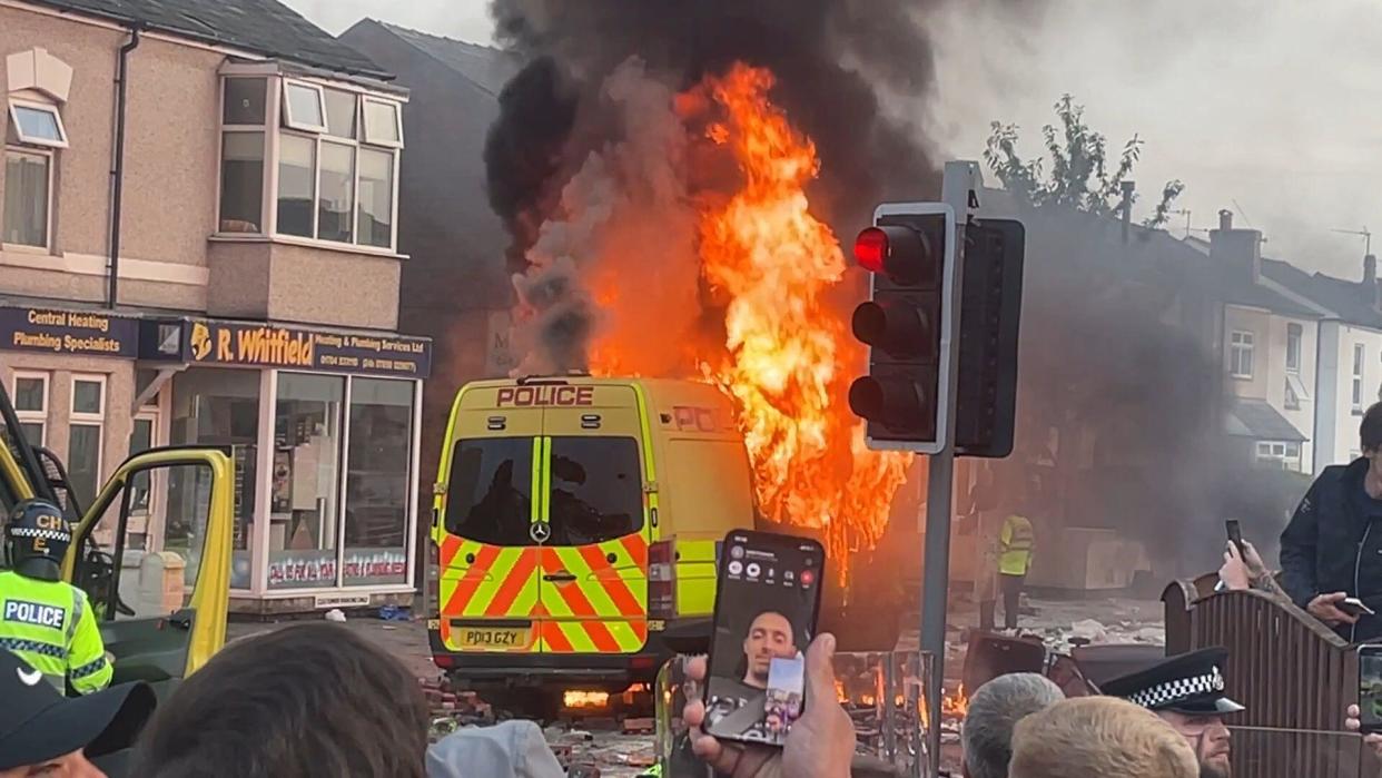 A police van set alight as trouble flares during a protest in Southport, after three children died and eight were injured in a 