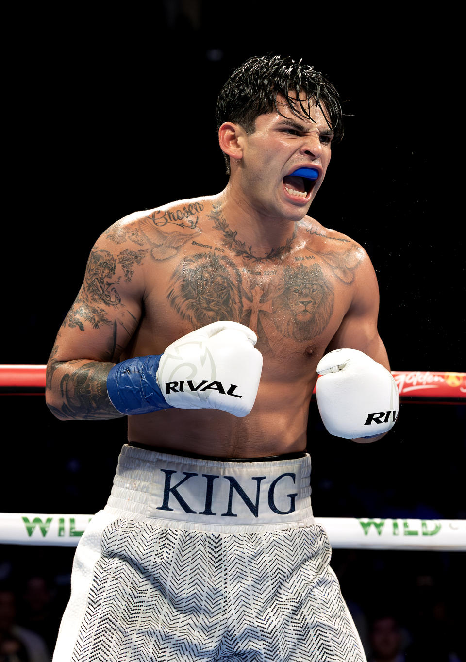 Ryan Garcia wearing boxing gloves and shorts "king" Written on waistband shouting in boxing ring during match