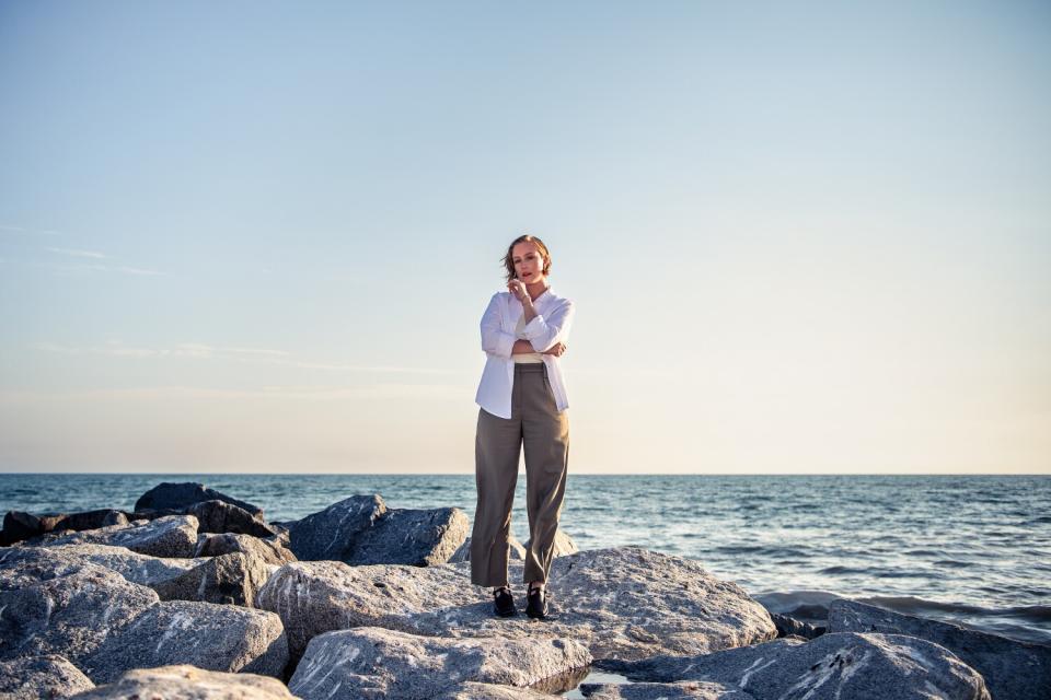 Hannah Einbinder stands on a rocky outcropping near the ocean.