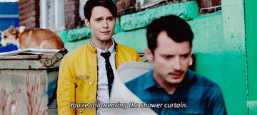 A man in a yellow jacket yells at another man wrapped in a shower curtain