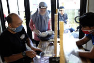 A staff in protective gears serves customers sitting separated by a plastic sheet barrier installed to help curb the new coronavirus outbreak at a coffee shop in Makassar, South Sulawesi, Indonesia, Sunday, May 31, 2020. (AP Photo/Masyudi S. Firmansyah)