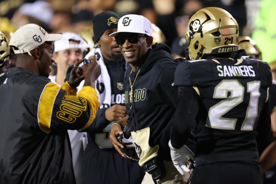 Colorado coach Deion Sanders smiles as his son, Deion Sanders Jr., films his celebration with safety Shilo Sanders