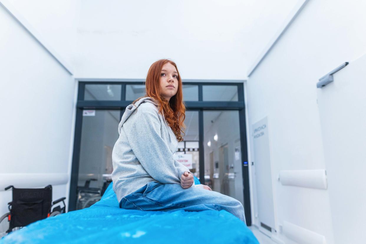 Scared girl sitting on hospital stretcher, waiting for examination in hospital after car accident, crash. Waiting for ER doctor in emergency room.