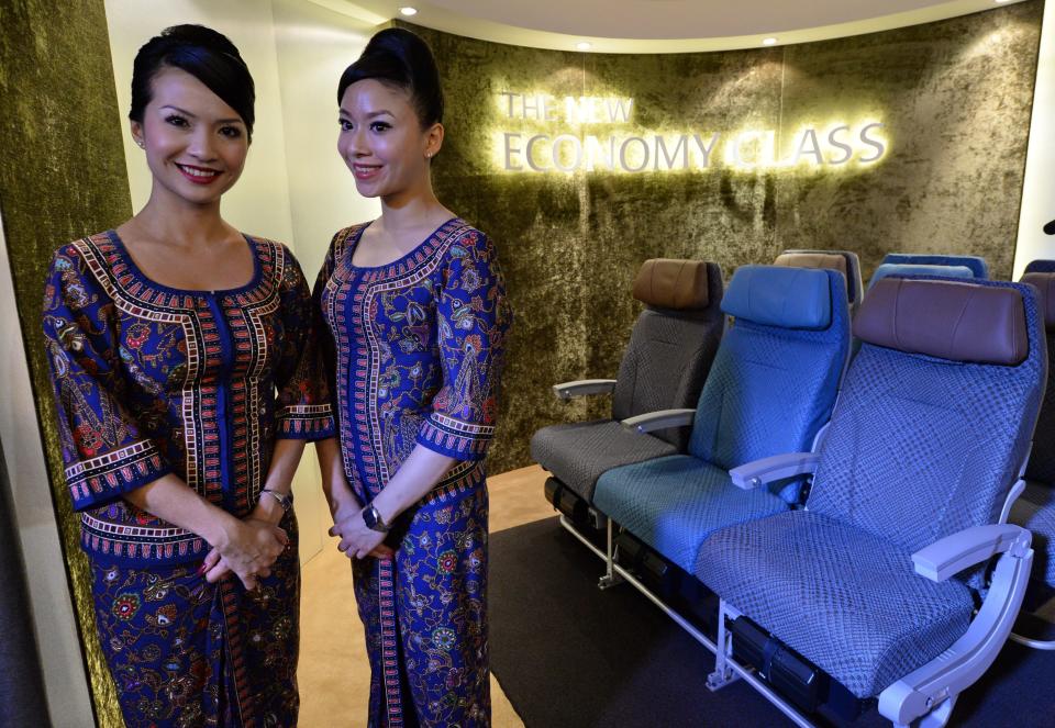 A Singapore Airlines (SIA) stewardesses stand next to a display of the new Singapore Airlines Economy Class seats during their next generation cabin product launch in Singapore on July 9, 2013. SIA on July 9 unveiled new seats and other in-flight amenities as part of a sweeping upgrade of its cabins amid intensifying competition in the industry. AFP PHOTO / ROSLAN RAHMAN