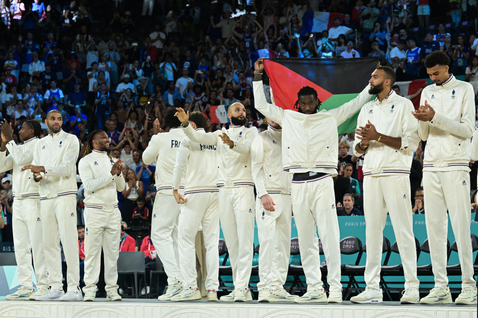 Silver medallists France's #26 Mathias Lessort (C-R), holding the flag of the French overseas department and region of Martinique, and teammates pose on the podium after the men's Gold Medal basketball match between France and USA during the Paris 2024 Olympic Games at the Bercy Arena in Paris on August 10, 2024. (Photo by Damien MEYER / AFP) (Photo by DAMIEN MEYER/AFP via Getty Images)