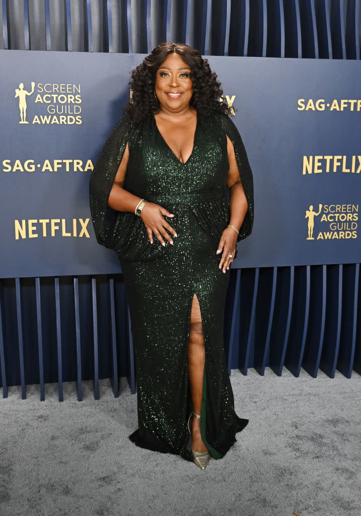 Loni Love poses in a glittery gown with sheer sleeves and a thigh-high slit