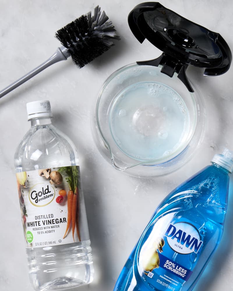 A coffee pot with vinegar and dish soap in it with a cleaning brush.