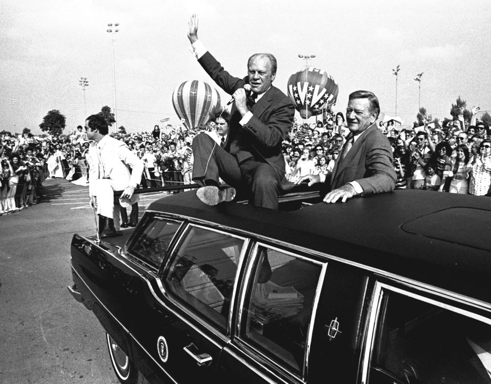 FILE - President Gerald Ford and actor John Wayne move through a crowd estimated at 23,000 at Fountain Valley, Calif., Oct. 24, 1976. Ford, a Republican, became president when Nixon stepped down, and he announced that he would run for a full term of his own on July 8, 1975. He had a 52% approval rating the month before. He faced discontent over inflation and controversy from his decision to pardon Nixon, and he lost the election to Jimmy Carter, a Democrat. (AP Photo, File)