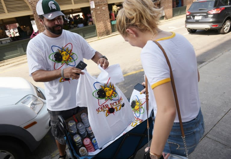 T-shirt vendor Jan Dahouas shows an eclipse t-shirt of his own design to a buyer on a street near the City Market in Charleston, South Carolina