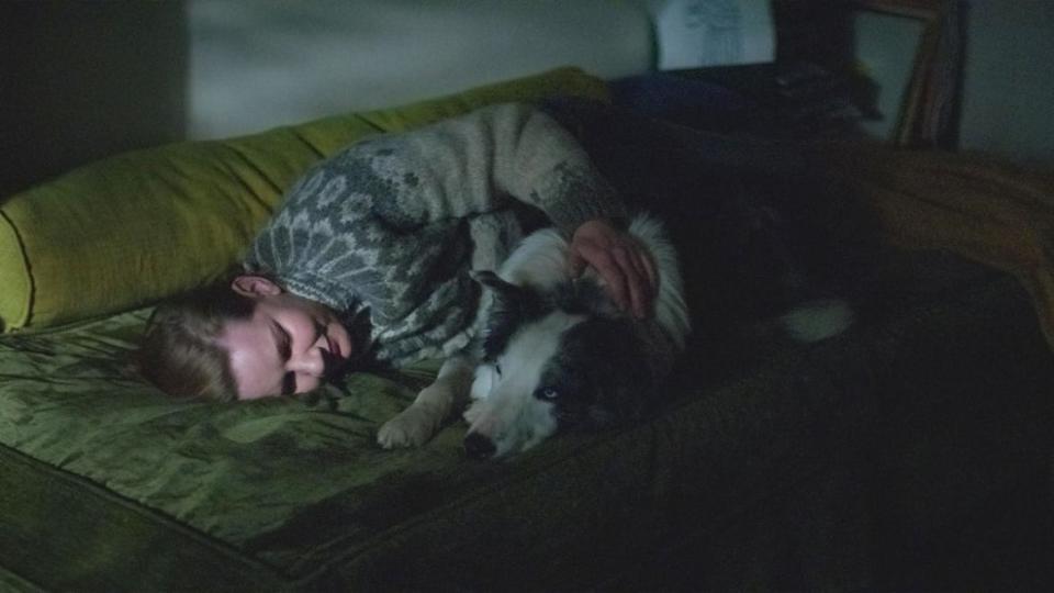 A woman lies on the couch with her dog.