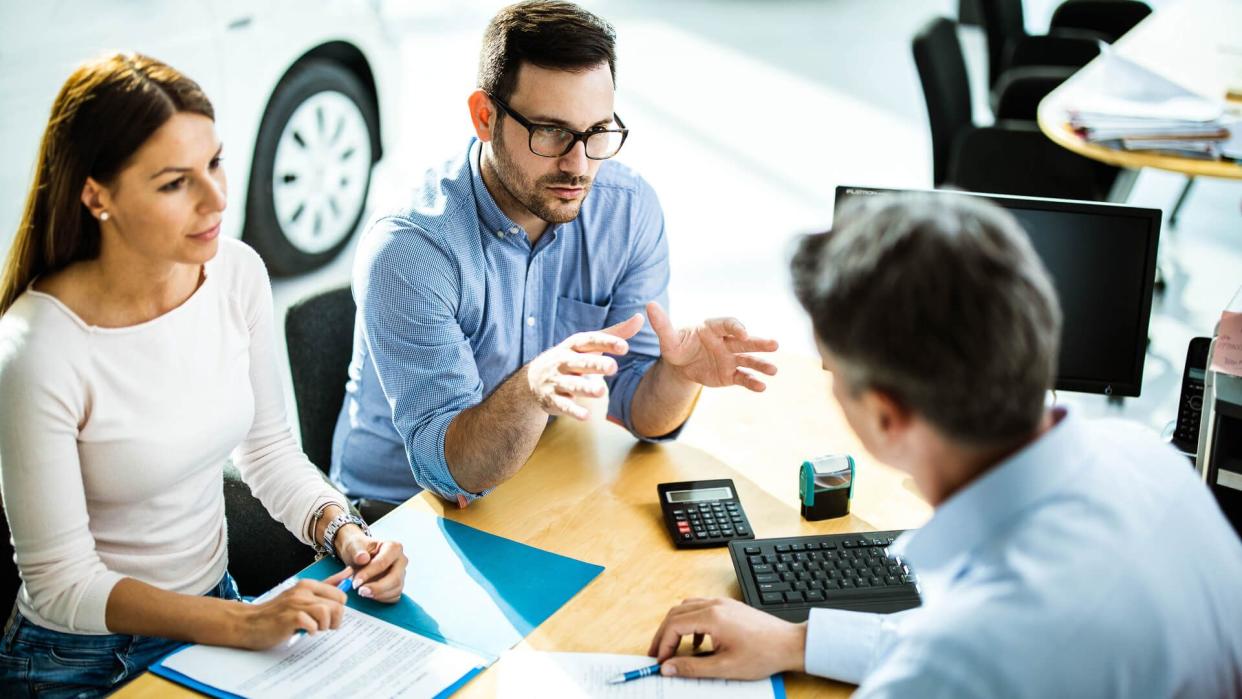 Above view of young couple communicating with car salesperson on a meeting in showroom.