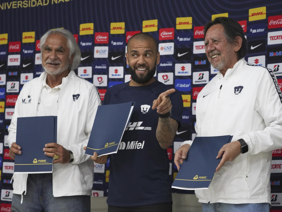 Flanked by Miguel Mejia Baron, UNAM's vice president of sports, left, and Leopoldo Silva, Pumas club president, right, Brazilian Dani Alves holds his contract during a press conference where he was presented as a new member of the Pumas UNAM soccer club, in Mexico City, Saturday, July 23, 2022. (AP Photo/Marco Ugarte)