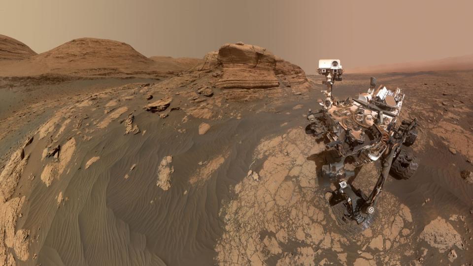 curiosity rover on mars next to a small reddish-brown hill