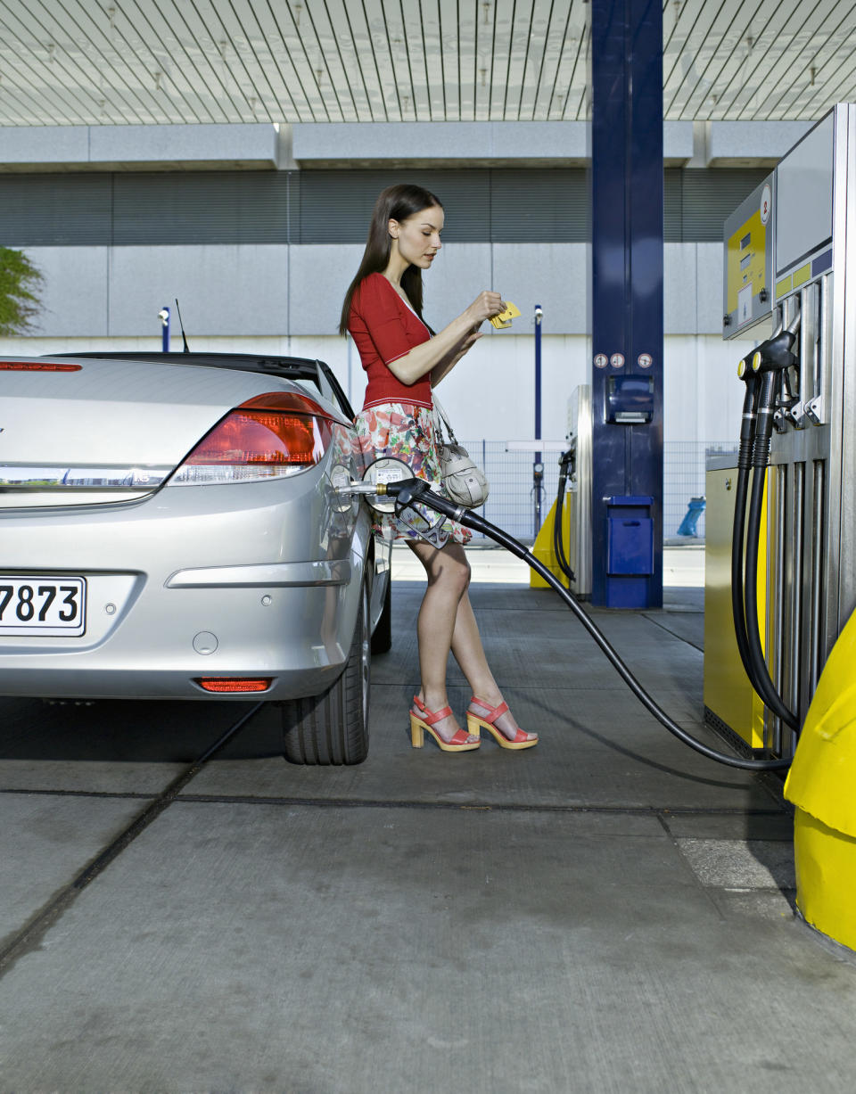 A woman leaning against her car as she pumps gas