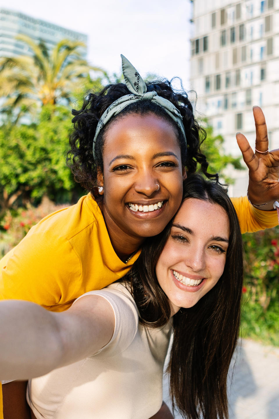 Two women smiling at the camera outdoors, one giving a peace sign