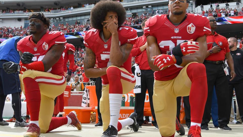 eli harold, colin kaepernick, and eric reid kneel on the sideline at a football game while wearing san francisco 49ers uniforms without helmets