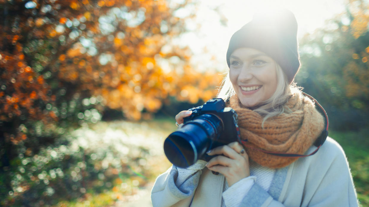 Smiling woman with digital camera in sunny autumn park.