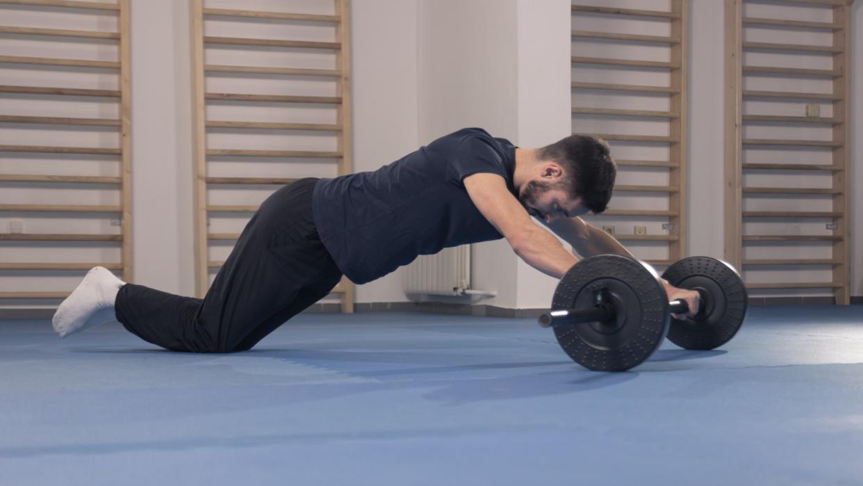  Man performing an ab rollout using a barbell in the gym  