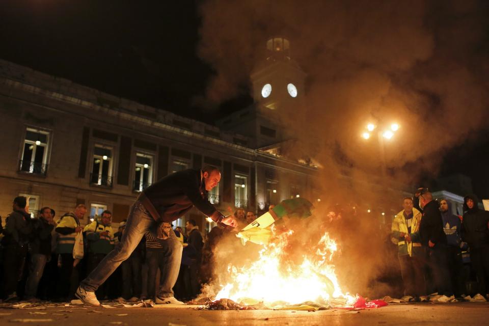 A cleaning worker throws his jacket to the fire during a protest at Madrid's Puerta del Sol square November 4, 2013. Spain's labor unions called for an indefinite strike from Tuesday in Spain's capital for the street cleaning and park maintenance sectors in protest against announced layoffs that could affect around a thousand municipal workers, according to local media. (REUTERS/Juan Medina)