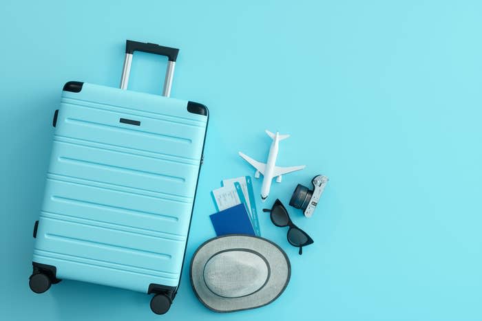 A suitcase with a hat, sunglasses, passport, and small airplane next to it