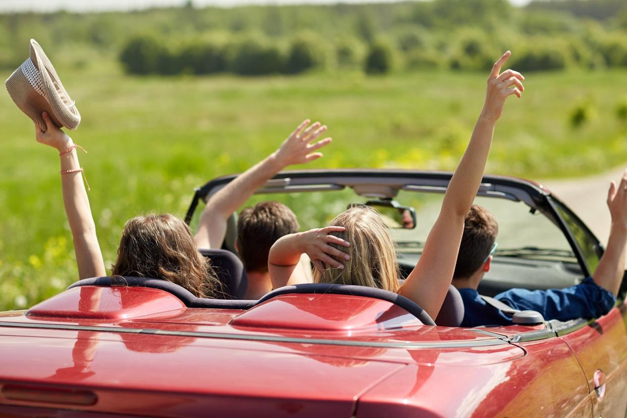 happy friends driving in cabriolet car at country and waving hands