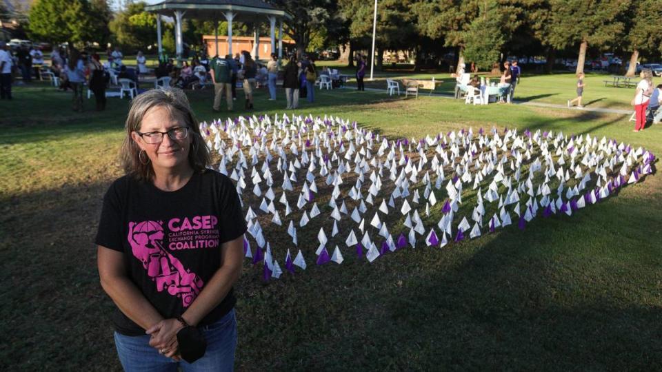Candace Winstead, SLO Bangers program coordinator and grant manager, stands at Mitchell Park in front of a heart made up of white flags that represent local overdose reversals and lives saved and purple flags that represent fatal drug overdoses. SLO Bangers works to reduce harm in San Luis Obispo County from the opioid crisis and increasing overdoses.