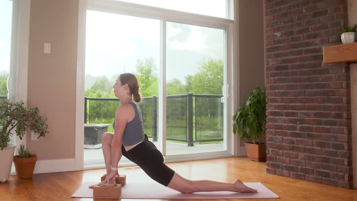 Woman on a yoga mat in a low lunge during a 20-minute power yoga class with her hands on blocks.