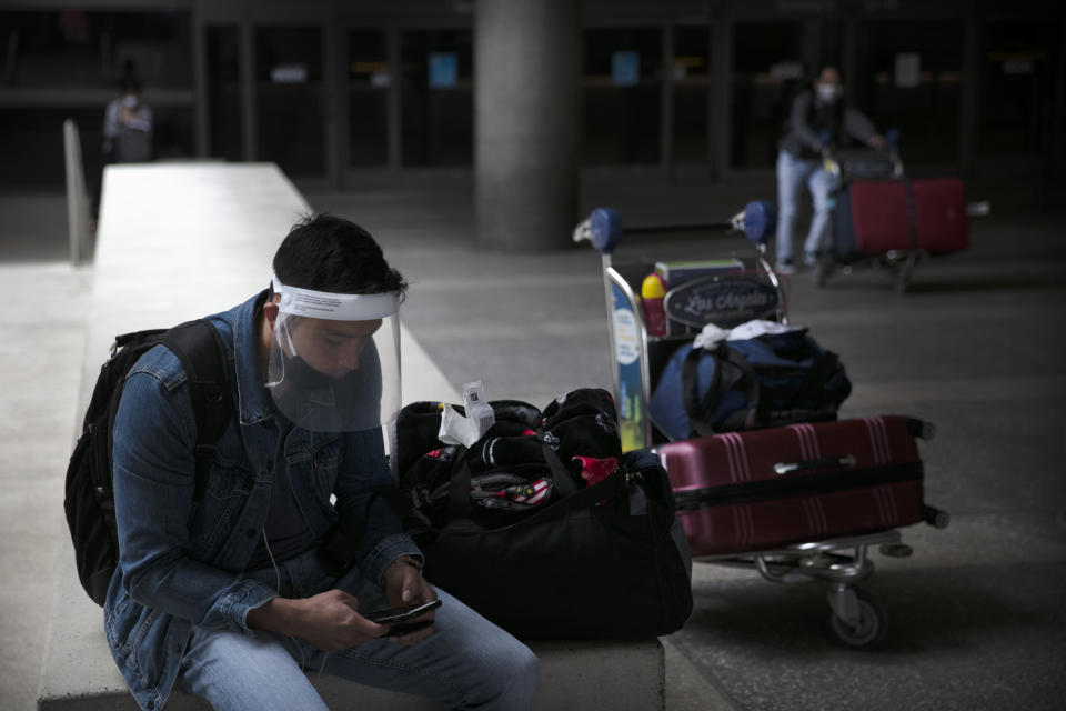 A traveler wearing a face shield looks at his phone outside the arrivals area at Los Angeles International Airport on Wednesday, June 24, 2020, in Los Angeles. The United States recorded a one-day total of 34,700 new COVID-19 cases, the highest in two months, according to the count kept by Johns Hopkins University. (AP Photo/Jae C. Hong)