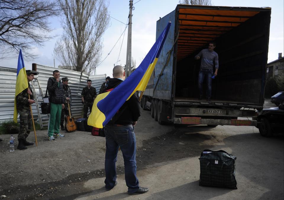 Ukrainian servicemen hold Ukrainian flags as they load their things into a truck leaving the Belbek airbase near Sevastopol, Crimea, Friday, March 28, 2014. Ukraine started withdrawing its troops and weapons from Crimea, now controlled by Russia. Russia's president says Ukraine could regain some arms and equipment of military units in Crimea that did not switch their loyalty to Russia. (AP Photo/Andrew Lubimov)