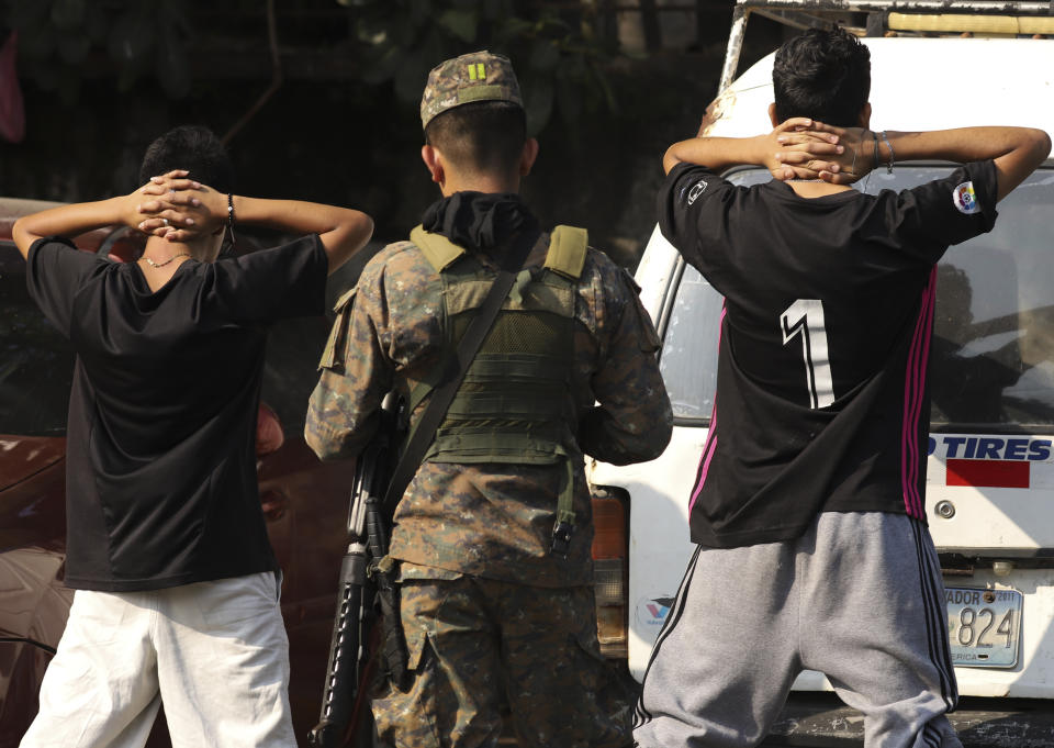 A soldier checks the identification of youths on the main street of La Campanera neighborhood in Soyapango, El Salvador, Sunday, March 5, 2023. Here in La Campanera, once one of the most bloody neighborhoods of the country, police and soldiers demand men strip off their shirts to examine their bodies for tattoos, and flip through deeds or energy bills for any evidence to show they weren’t part of Barrio 18, the gang that once dominated the zone. (AP Photo/Salvador Melendez)