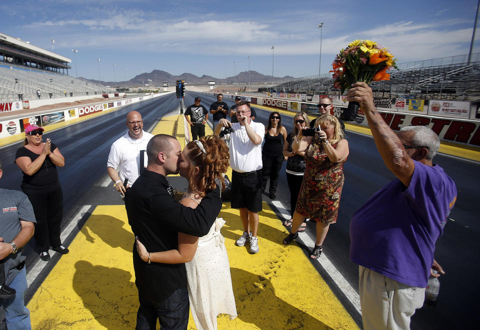 LAS VEGAS - OCTOBER 6: The Las Vegas Wedding Wagon's the Rev. Andy Gonzalez (2nd L) officiates a wedding between Josh Davis and Martha Arrey of California as the Rev. James Cass takes pictures at the drag racing strip at the Las Vegas Motor Speedway on October 6, 2012 in Las Vegas, Nevada. For USD 99, ordained ministers will drive a van with an altar to any location in and around Las Vegas and perform a legal wedding, vow renewal or commitment ceremony in about 10 minutes. The fee includes wedding photos but not a marriage license. Couples can either get hitched at the Wedding Wagon's walk-up window or at iconic areas including the Welcome to Fabulous Las Vegas sign, the fountains at the Bellagio, the Hoover Dam and pedestrian bridges overlooking the Las Vegas Strip. (Photo by Isaac Brekken/Getty Images)