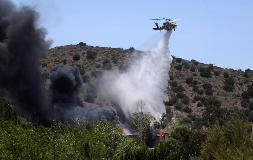 A firefighting helicopter makes a water drop on a house engulfed in fire, in Acton, Calif., on Tuesday, June 1, 2021. Los Angeles County Fire Department supervisor Leslie Lua said paramedics responded to reports of gunshots shortly before 11 a.m. at Fire Station 81, about 45 miles (72 kilometers) north of Los Angeles. Around the time of the shooting, a fire broke out at the home less than 10 miles (16 kilometers) east of the station and police swarmed the area. TV helicopter reporters said a body that may be the gunman was visible outside the home, which was gutted by flames in about three hours. (AP Photo/David Swanson)