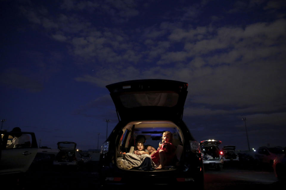 A family watches a movie from the back of their car at a drive-in movie theater where drivers must leave one space empty between them amid the new coronavirus pandemic in Brasilia, Brazil, Saturday, May 23, 2020. The drive-in is 47 years old and one of the only such open-air facilities in operation in Brazil. (AP Photo/Eraldo Peres)